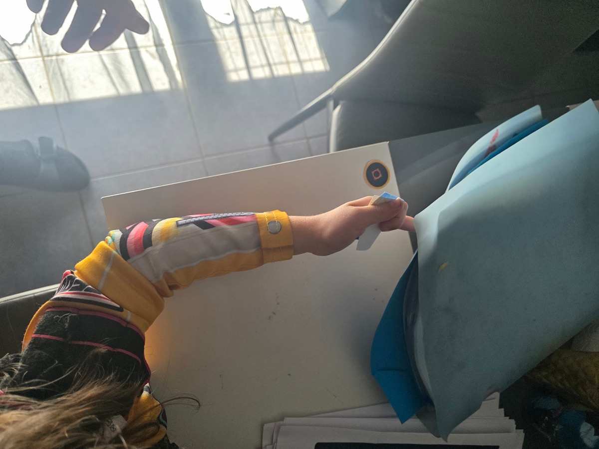 Une petite fille soulève une feuille sur la table et découvre la pastille cachée en dessous.