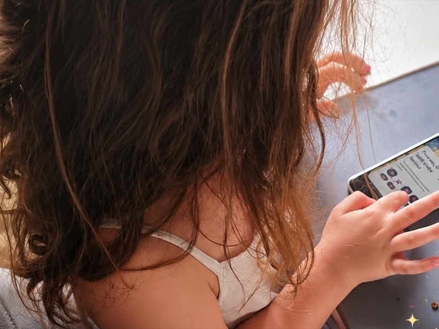 Une enfant vue de dos, penchée sur un téléphone posé sur une table, en train de suivre une aventure Quézo.